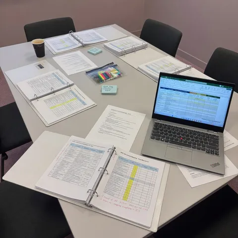 Compliance binders, control matrices, and a laptop on a conference table during a framework mapping review